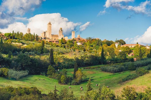Aerial view of San Gimignano's medieval towers and terracotta rooftops surrounded by rolling green Tuscan countryside, Tuscany walking holiday, Italy
